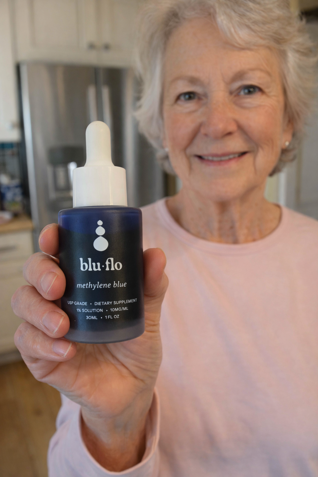 Older woman holding a blu flo methylene blue supplement bottle in a kitchen setting