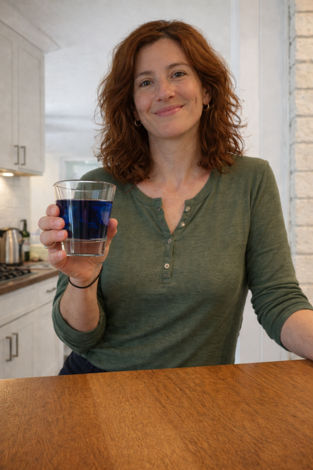 Woman holding a glass of methylene blue liquid in a kitchen