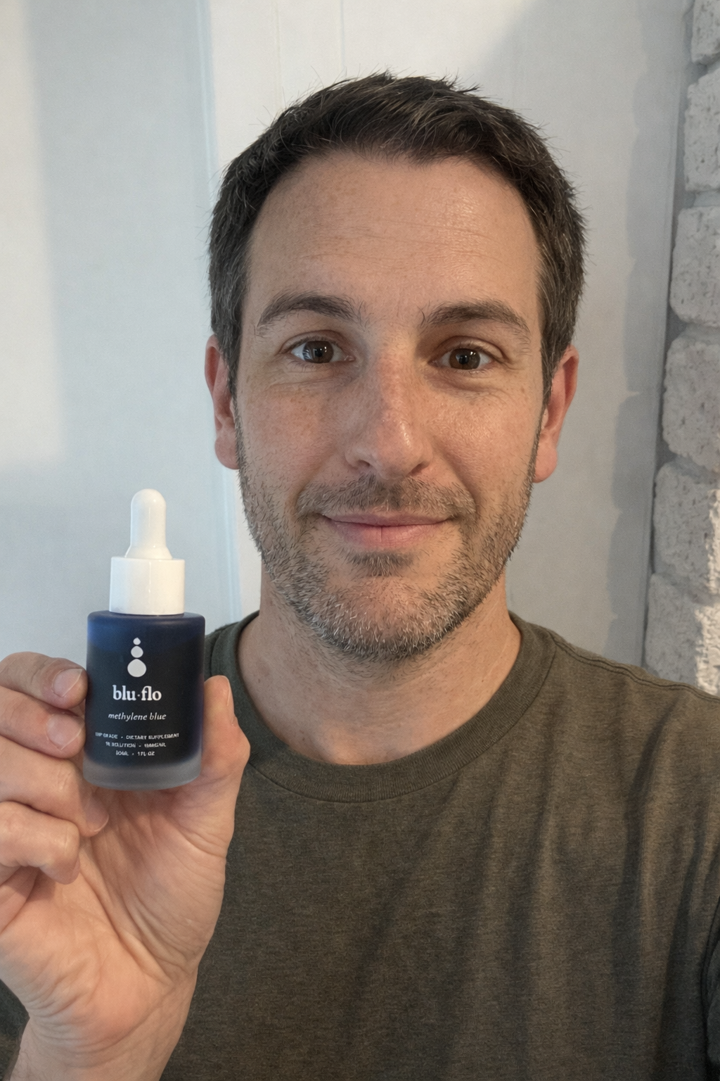 Man holding a blue bottle of methylene blue labeled 'blu flo' against a neutral background